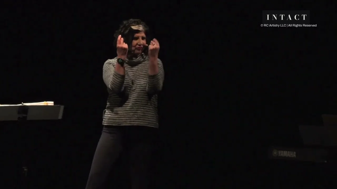 Robin Colucci performing Intact in a striped top, hands at her temples
