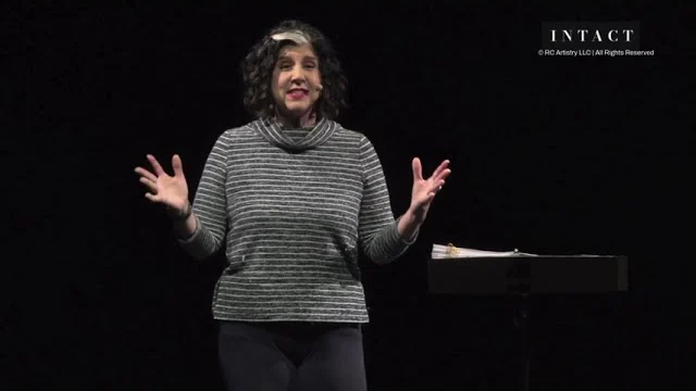 Robin Colucci in a striped top, hands raised mid-story on the Theatre Row stage